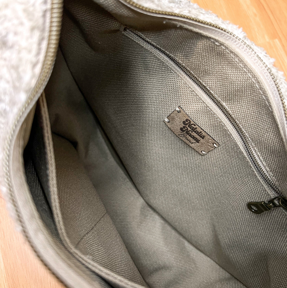 Close-up of the interior of a gray textured bag with a zippered pocket and a metal brand plaque reading 'Siberian Wolf'.
