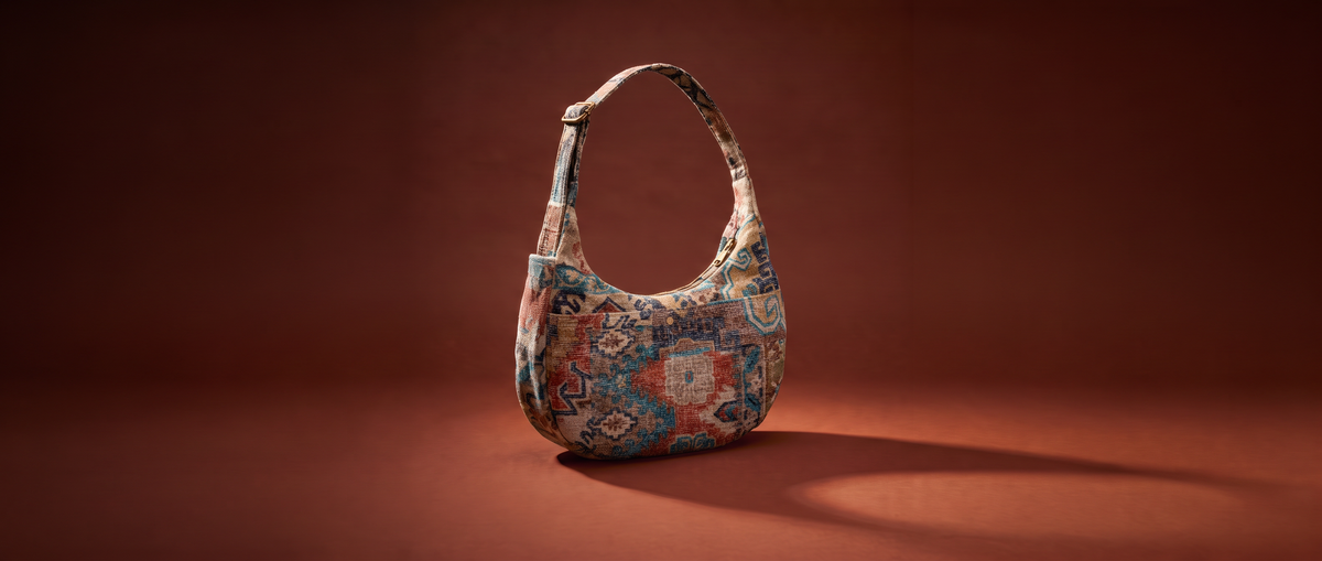 A hobo-style shoulder bag with a colorful, distressed geometric and floral pattern, standing upright on a dark brown studio background.