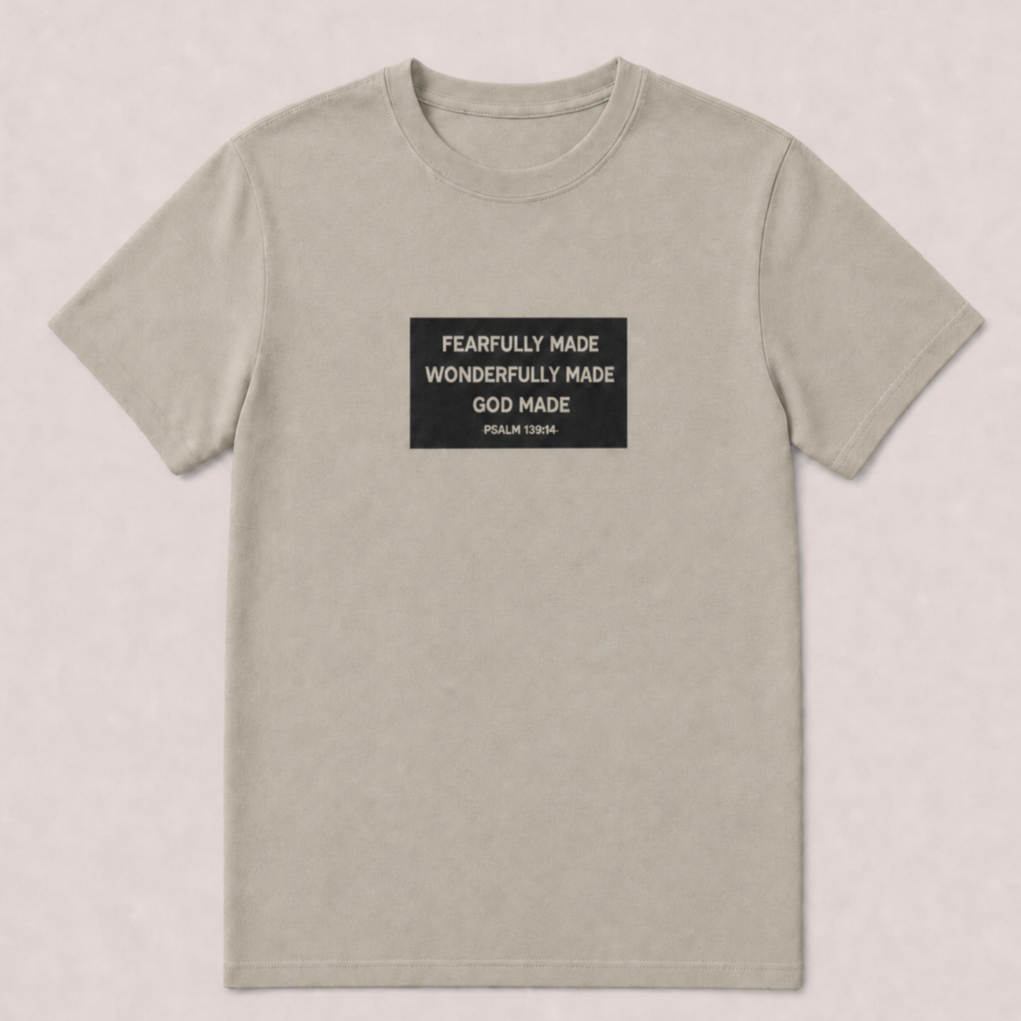 A light beige crewneck t-shirt with a black rectangular graphic on the chest containing white text that reads 'FEARFULLY MADE WONDERFULLY MADE GOD MADE PSALM 139:14'.
