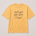 A yellow short-sleeve t-shirt with the text 'Just a girl after God's heart' printed in black script on the front, displayed flat against a light gray background.