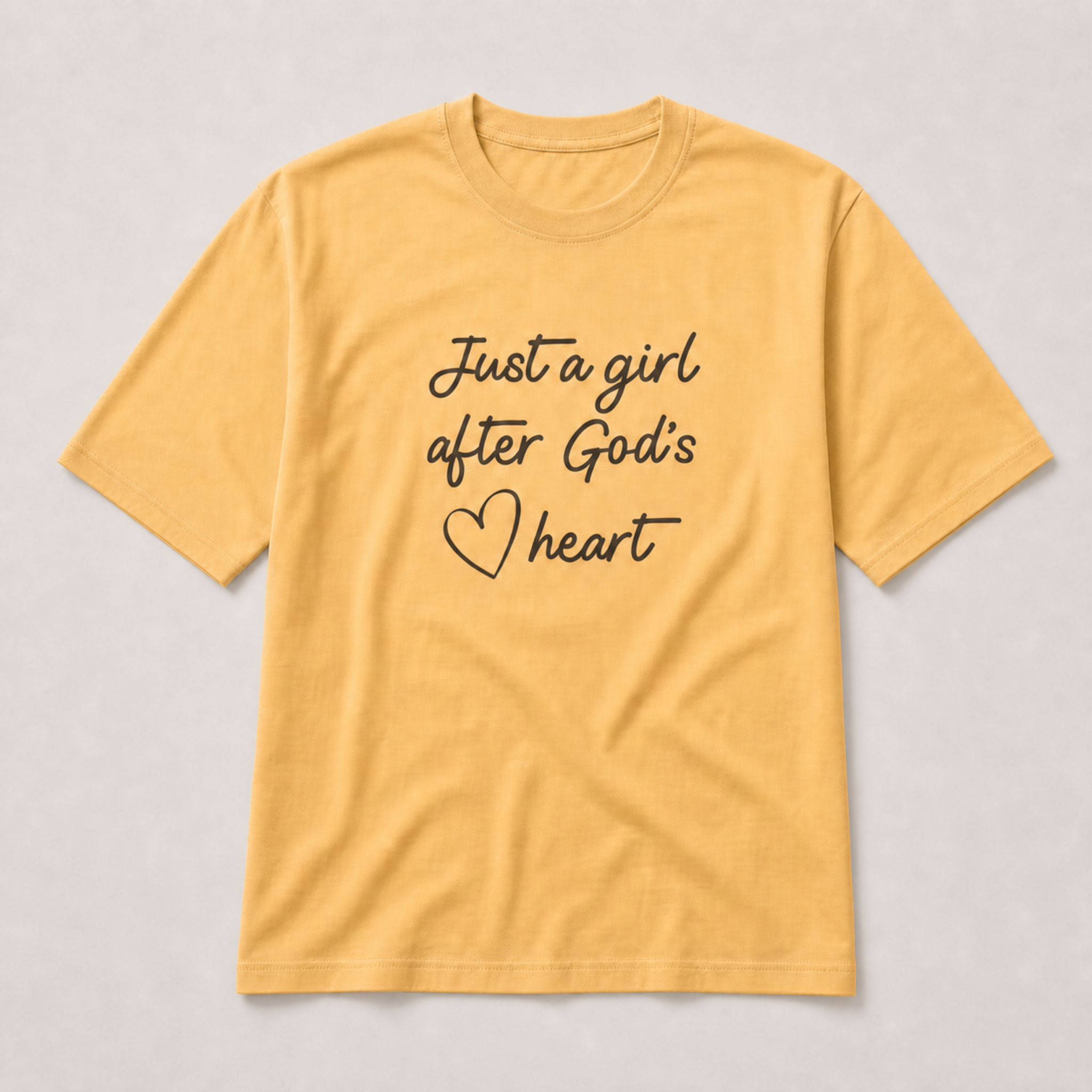 A yellow short-sleeve t-shirt with the text 'Just a girl after God's heart' printed in black script on the front, displayed flat against a light gray background.