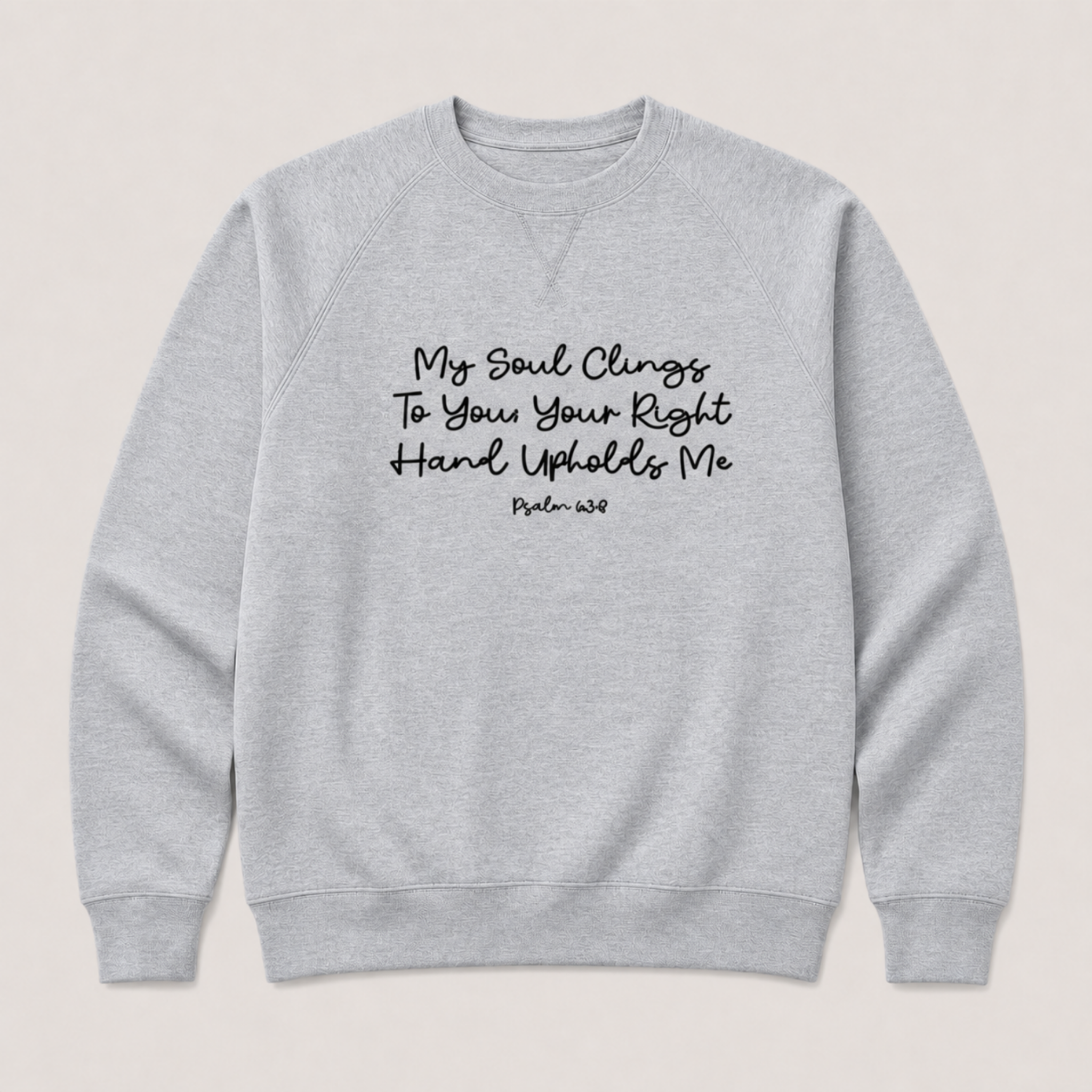 A light heather gray crewneck sweatshirt with black printed text on the chest reading 'My Soul Clings To You Your Right Hand Upholds Me Psalm 63:8' on a light beige background.