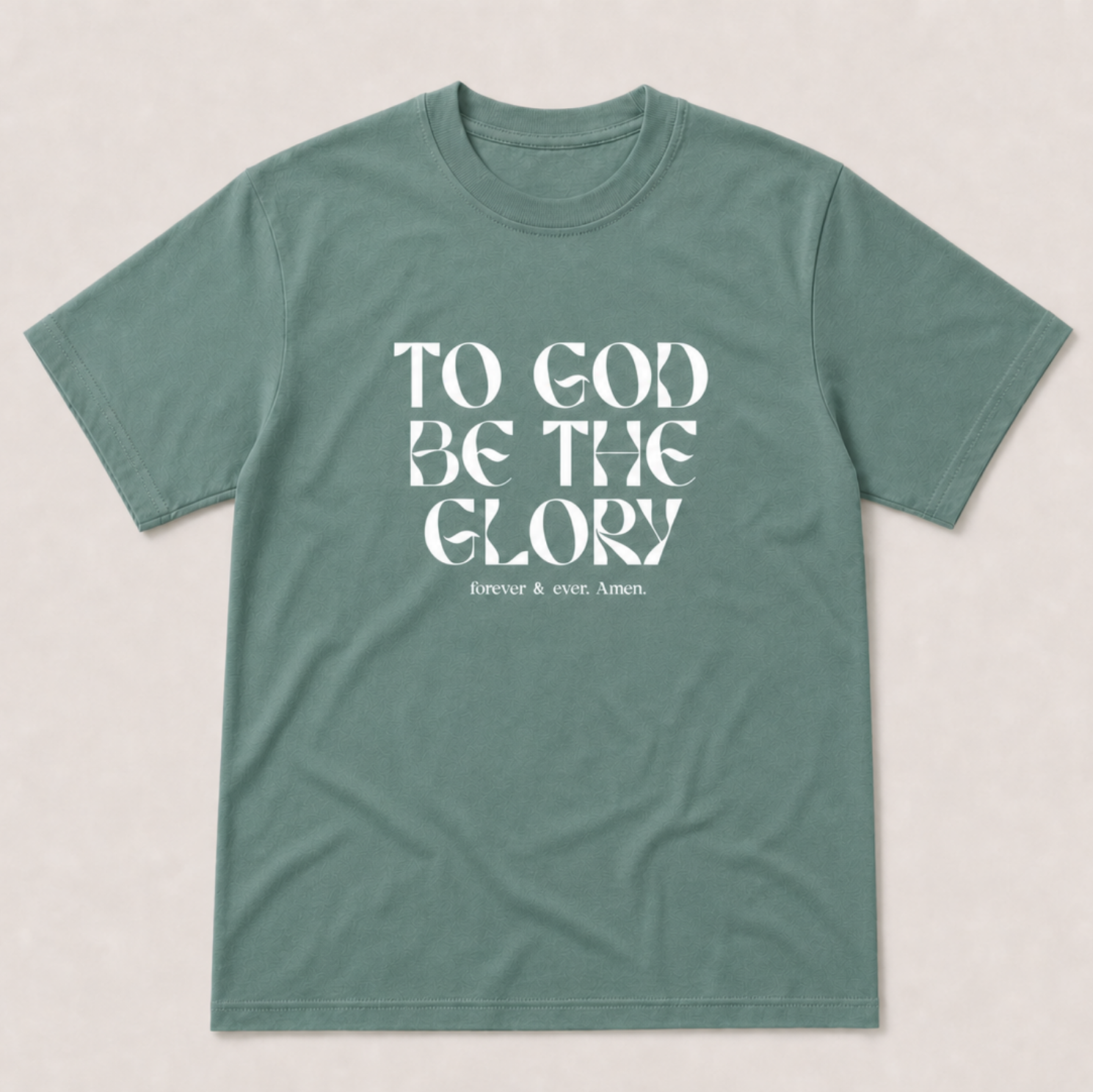 A sage green crewneck t-shirt with the text 'TO GOD BE THE GLORY' printed in white on the front, displayed flat against a light beige background.