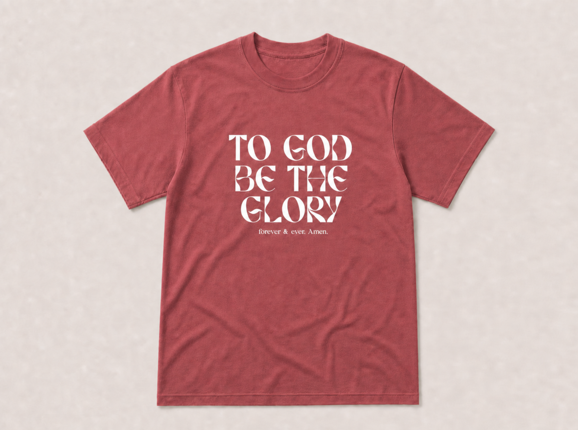 A heathered red crewneck t-shirt with the text 'TO GOD BE THE GLORY' printed in white on the front, displayed flat against a light beige textured background.
