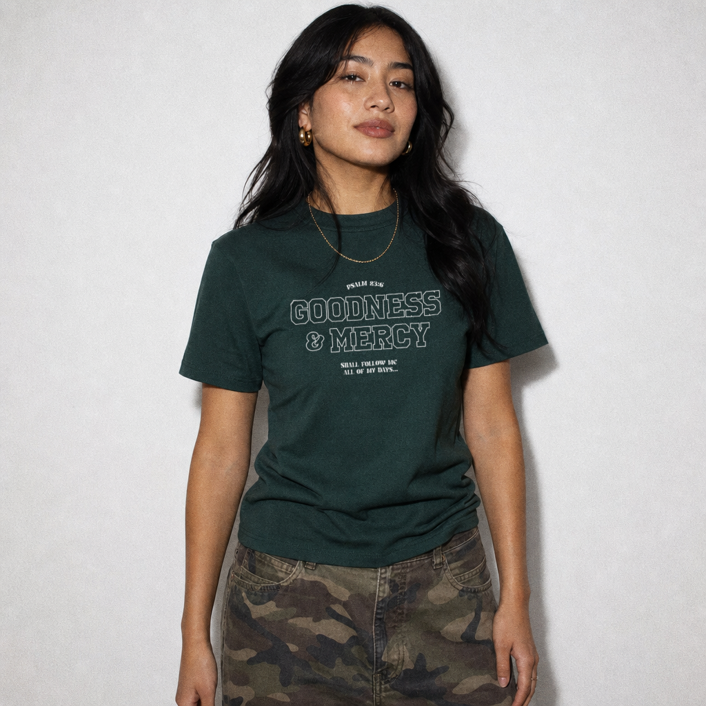 Person wearing a green t-shirt with 'GOODNESS & MERCY' text on a plain background